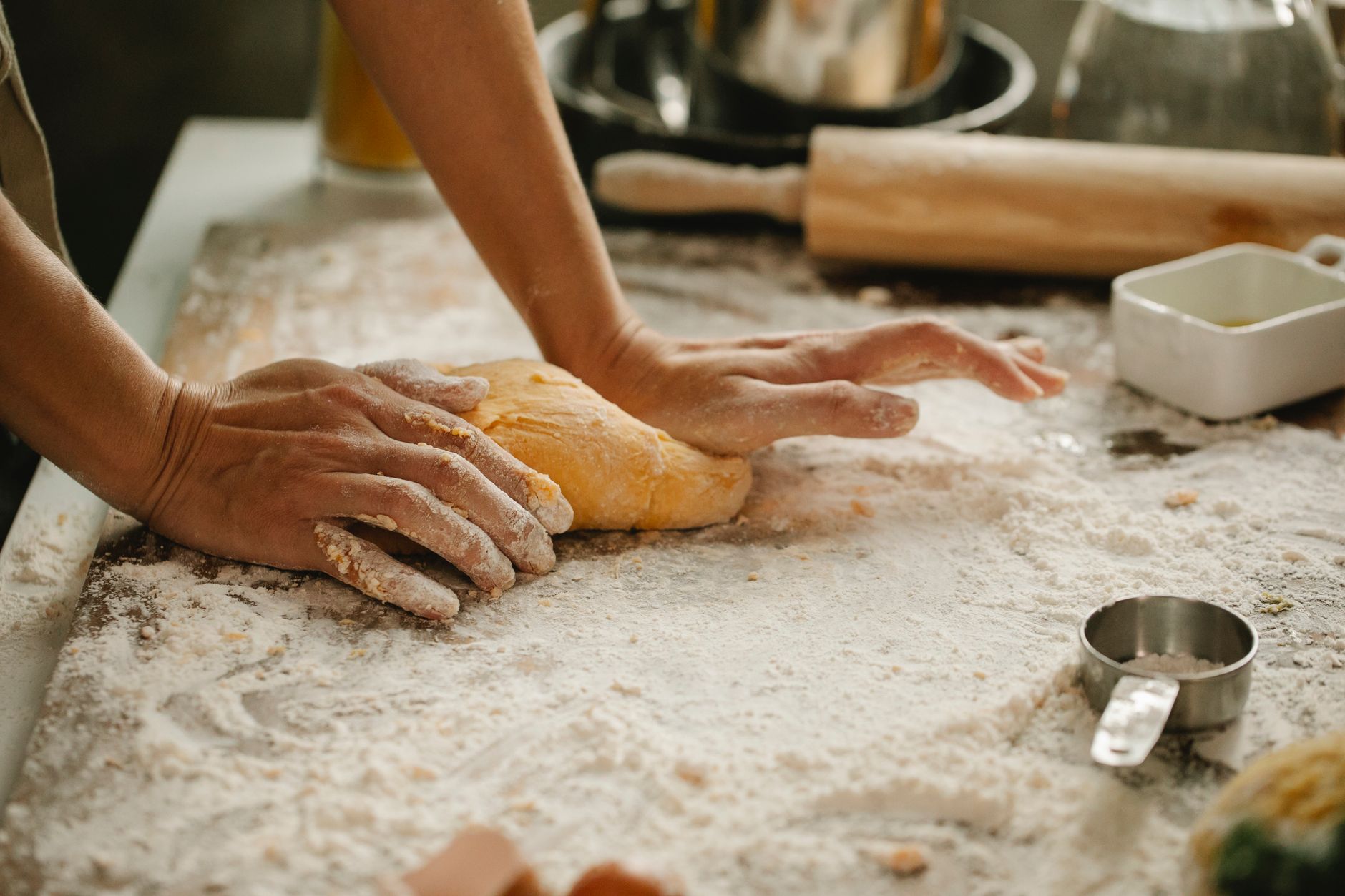 Bäckerinnenhände kneten frischen Teig auf einer bemehlten Holzfläche
